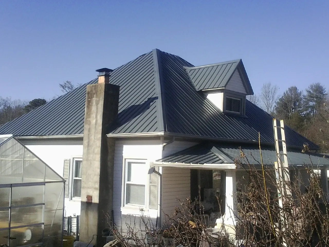 Dark blue standing seam metal roof on a white farmhouse with dormer — Slate & Tile Roof Repair by Roofing Brothers in Platte City