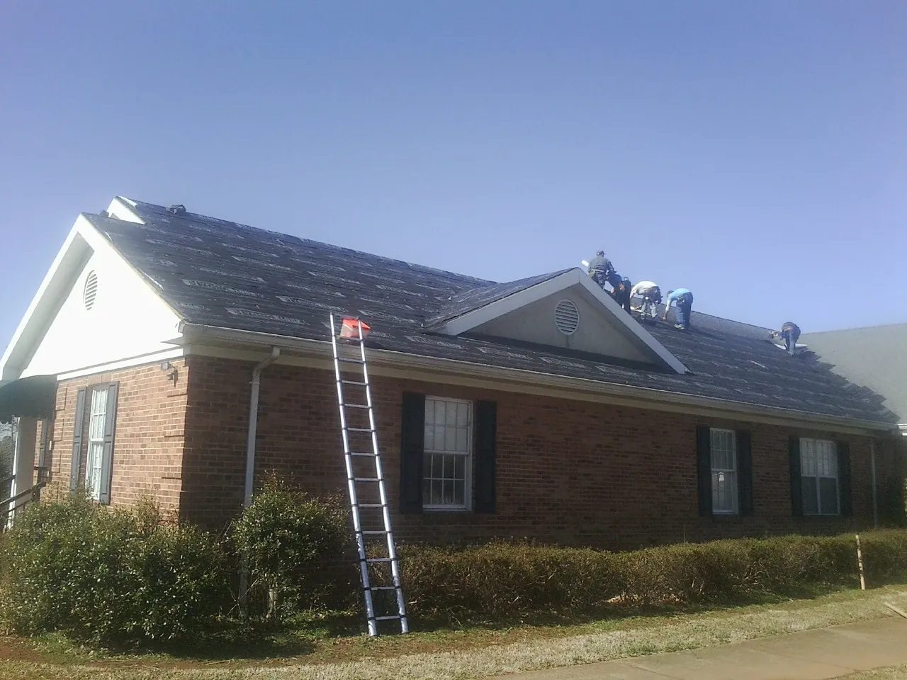 Crew tearing shingles off a brick ranch roof with a ladder set — Metal Roof Repair work by our crew in Platte City