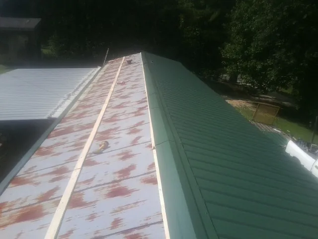 Old rusted panels beside newly installed green metal roofing — Wind Damage Roof Repair by Roofing Brothers in Platte City