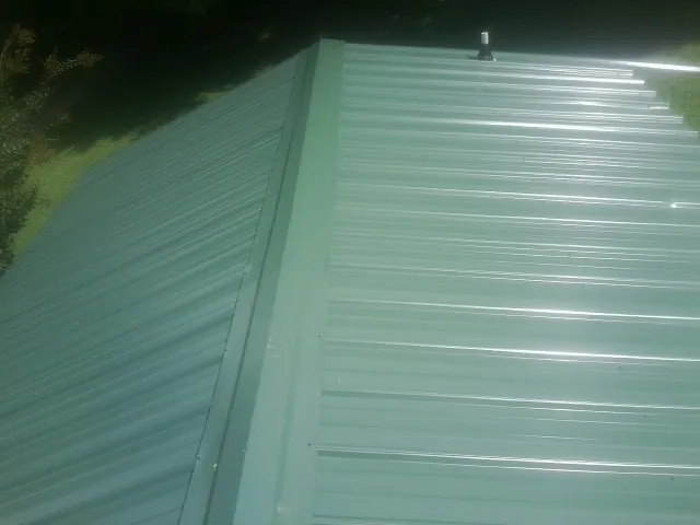 New green metal panels meeting at the ridge of a roof — Flat Roof Repair work by our crew in Platte City