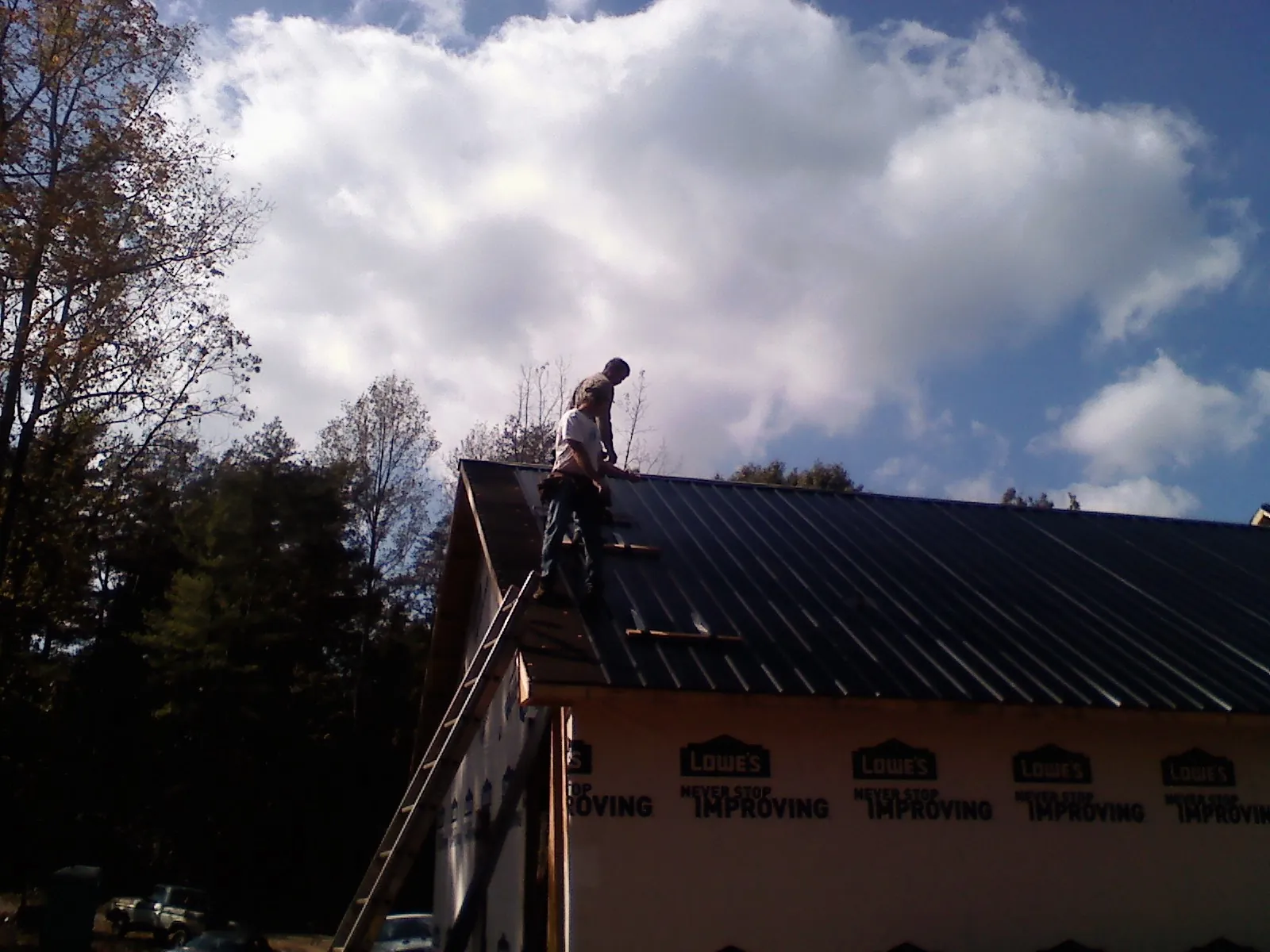 Roofer fastening dark metal panels high against a cloudy sky, from a Roof Inspection job in Platte City