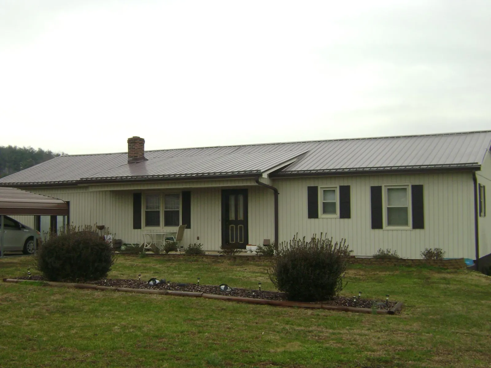 Brown metal roof on a cream sided ranch home with a brick chimney in Platte City