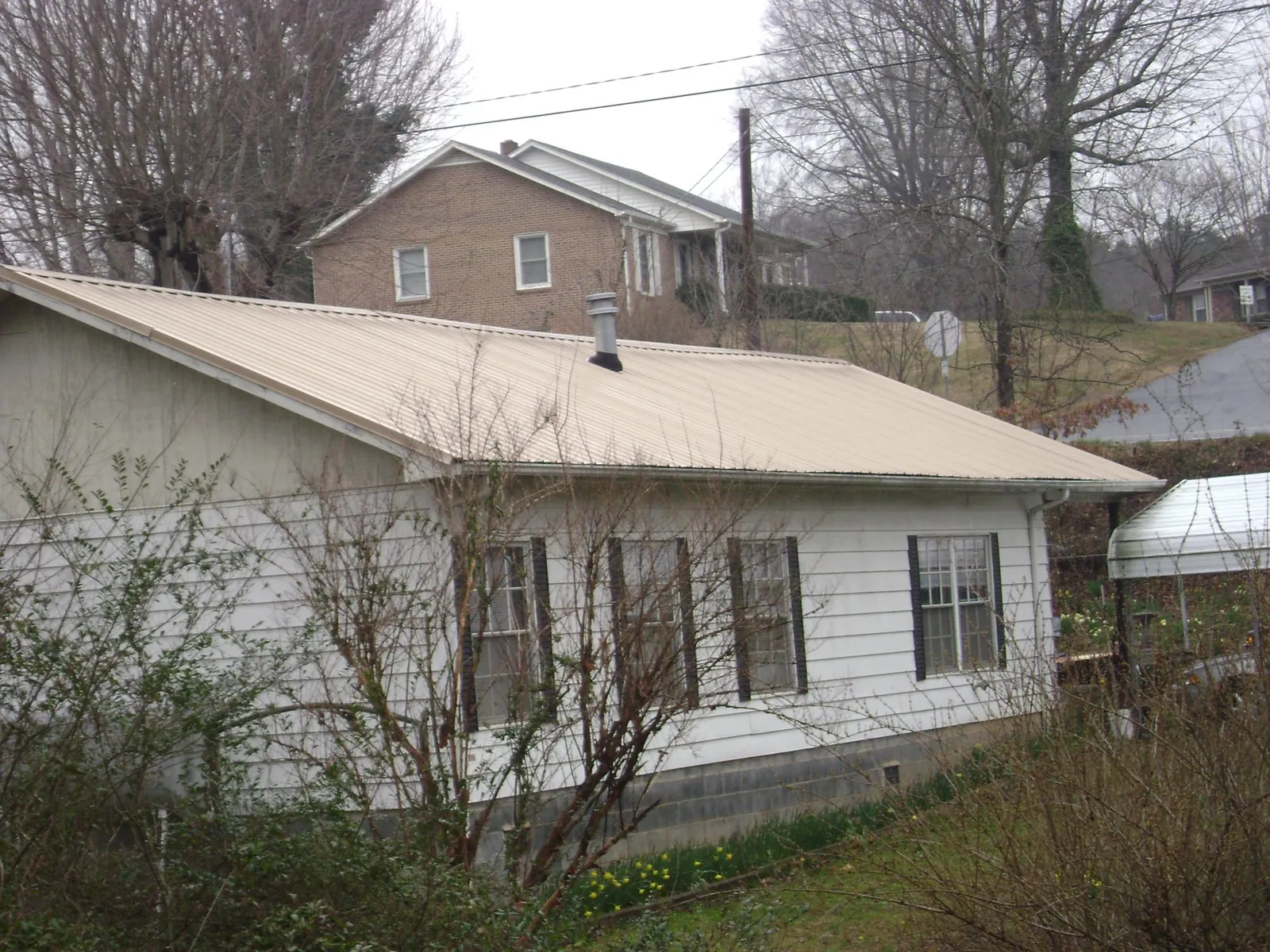 Tan metal roof on a white sided house set into a hillside — Commercial Roofing by Roofing Brothers in Platte City