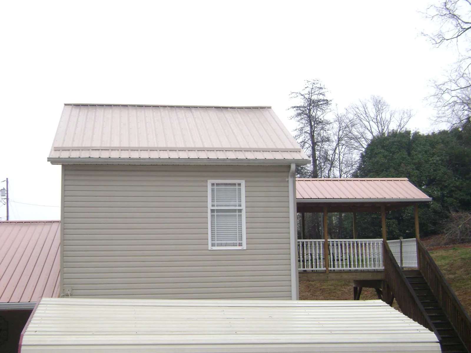 Tan metal roofs on a two story addition and attached porch, from a Roof Replacement job in Platte City